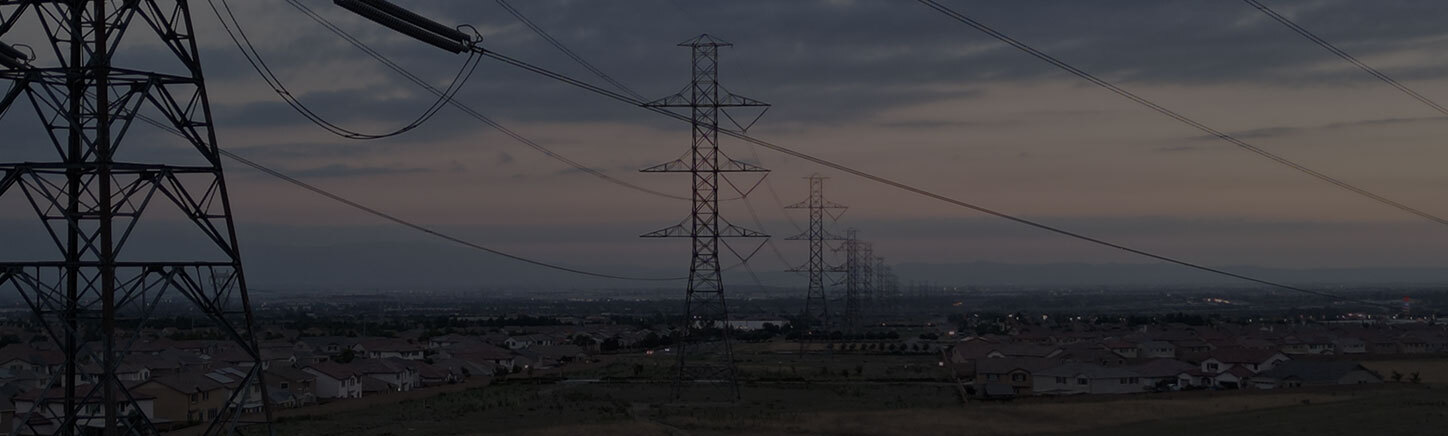 Aerial view of transmission power lines running near homes in city, showing utility infrastructure in a fire-prone region.