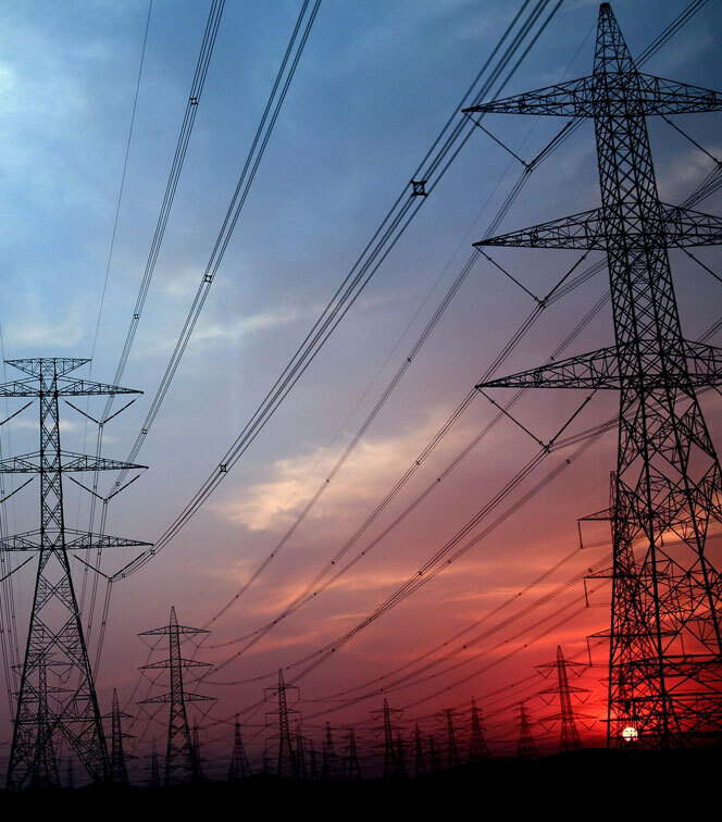 High-voltage power transmission towers and lines stretching across the landscape at sunset, silhouetted against a sky transitioning from blue to red.